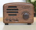 Compact vintage wood style Bluetooth speaker in pink, black, or wood grain finish on a table.
