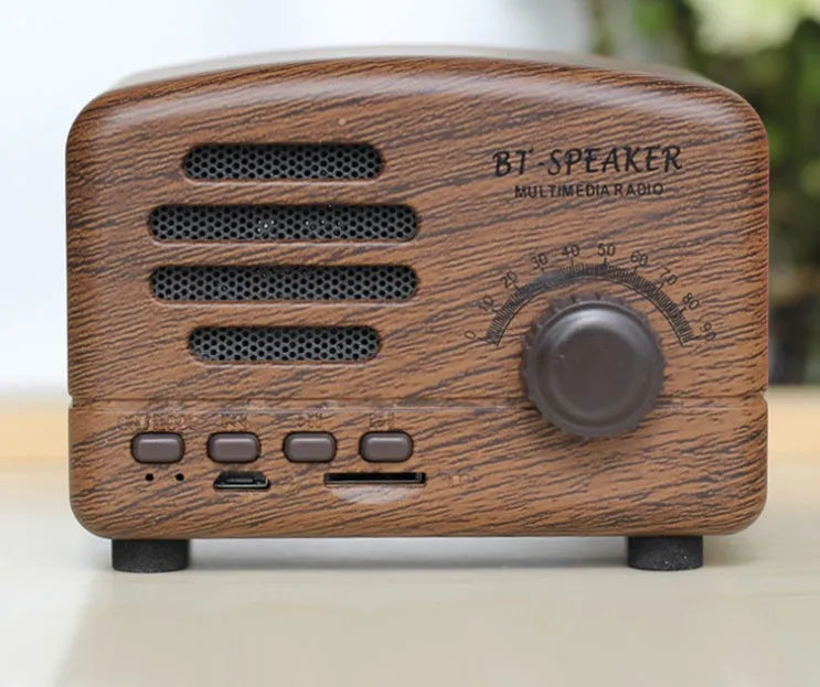 Compact vintage wood style Bluetooth speaker in pink, black, or wood grain finish on a table.