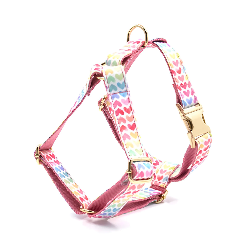 Pink dog harness with a gold buckle and a colourful heart-shaped stone on the chest strap.