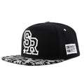 Cotton baseball cap with adjustable strap in black or white, showing embroidered letter detail on the front.