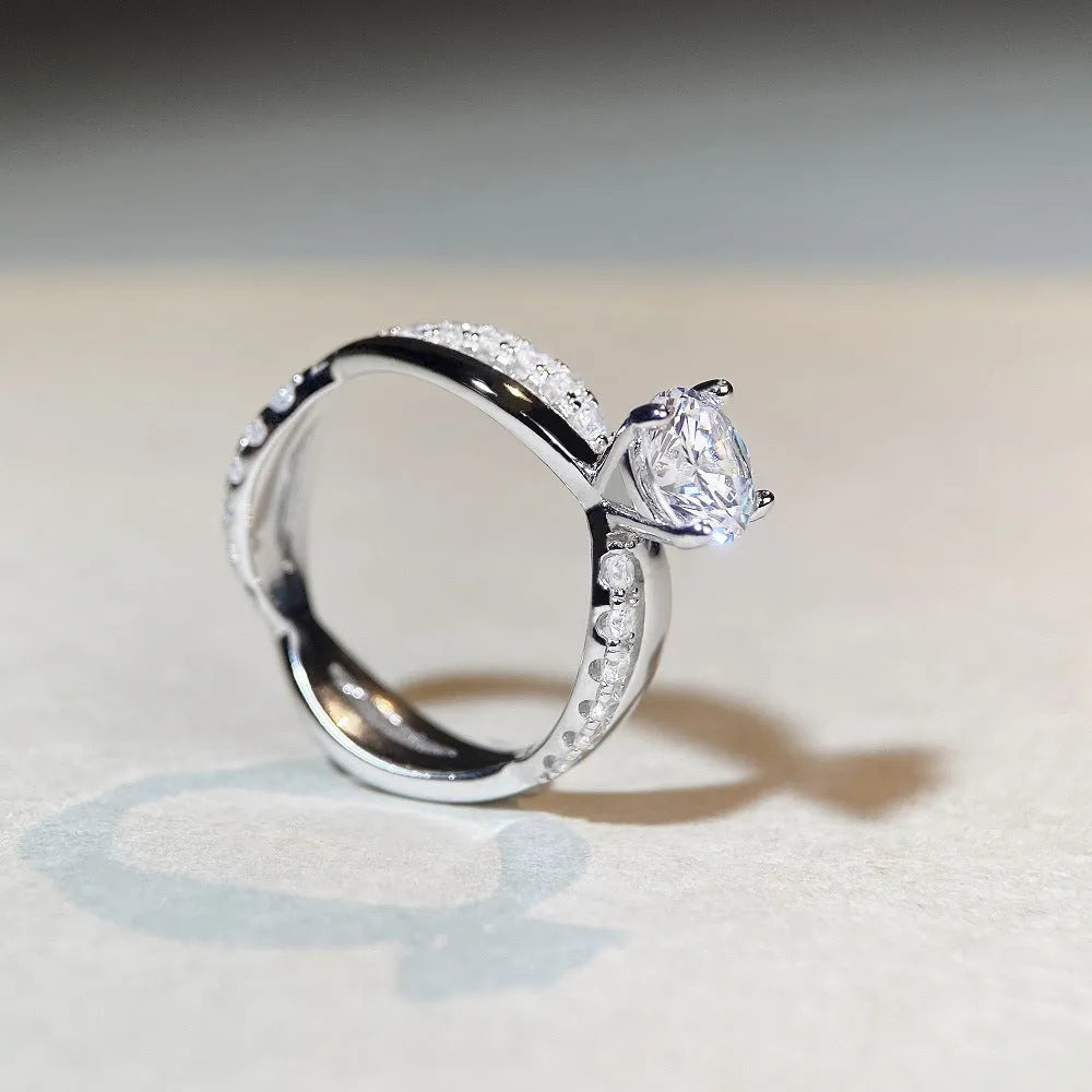 A silver moissanite ring with a 1 carat stone in a four-claw setting and a twisted geometric band.
