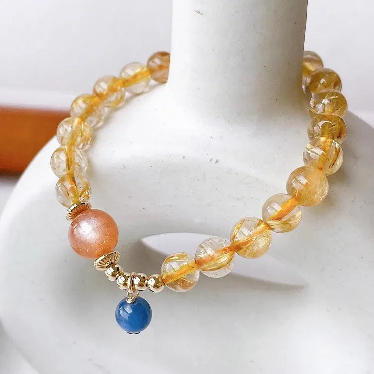 Gold rutilated quartz sunstone bracelet with diamond shapes and round beads on female wrist