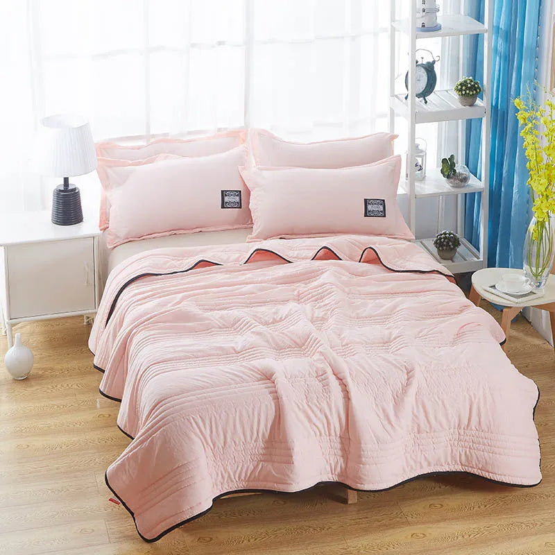 Plain colour seersucker summer cooling quilt shown in light pink on a bed.