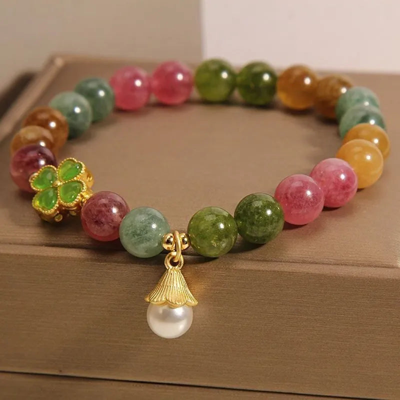 Natural colour tourmaline bracelet with four-leaf clover pearl pendant on wrist.