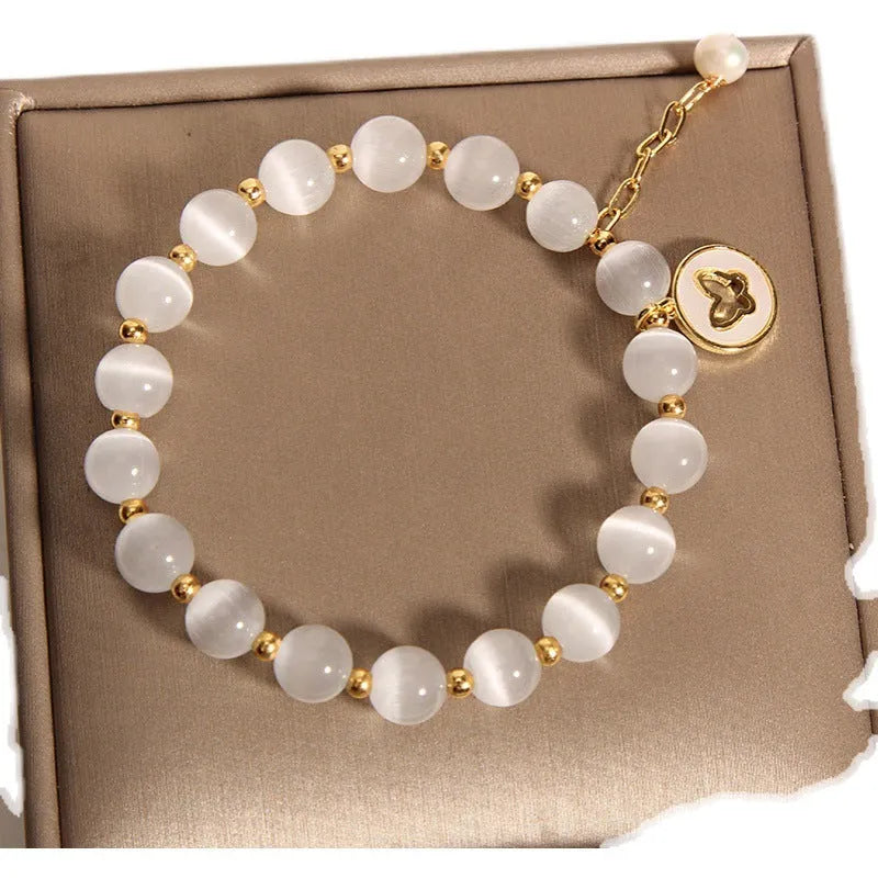 Close-up of a white cat's eye crystal bracelet with geometric links on a wrist.