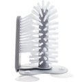 Grey 2-in-1 cup scrubber with double-sided bristles and three suction cups on a white surface