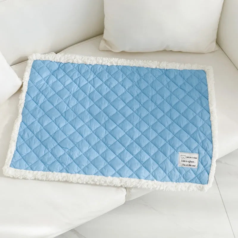 Blue quilted cloth pet blanket for cats lying flat, showing its rectangular shape and textured surface.