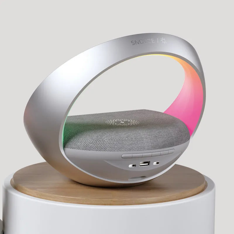 Beige multifunctional Bluetooth speaker with wireless charging pad, LED light, and digital clock display on wooden surface