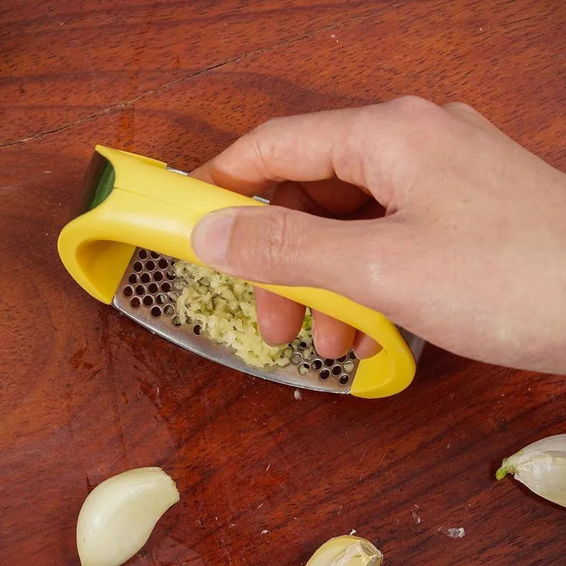 Stainless steel garlic press with ergonomic black handle on a kitchen counter.