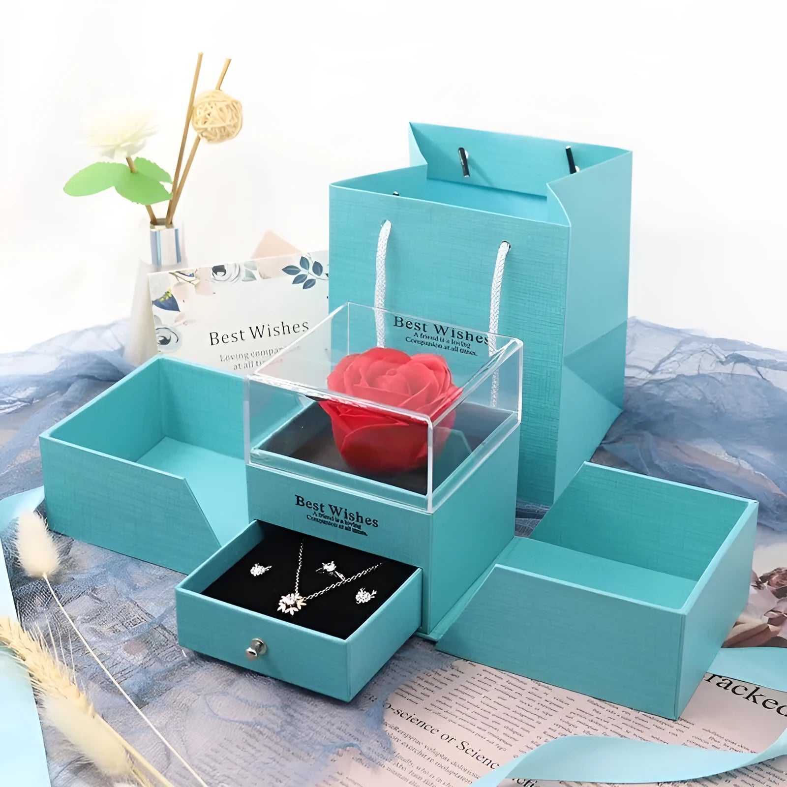 Blue jewellery gift box open with a plastic eternal rose inside, next to a pair of earrings.
