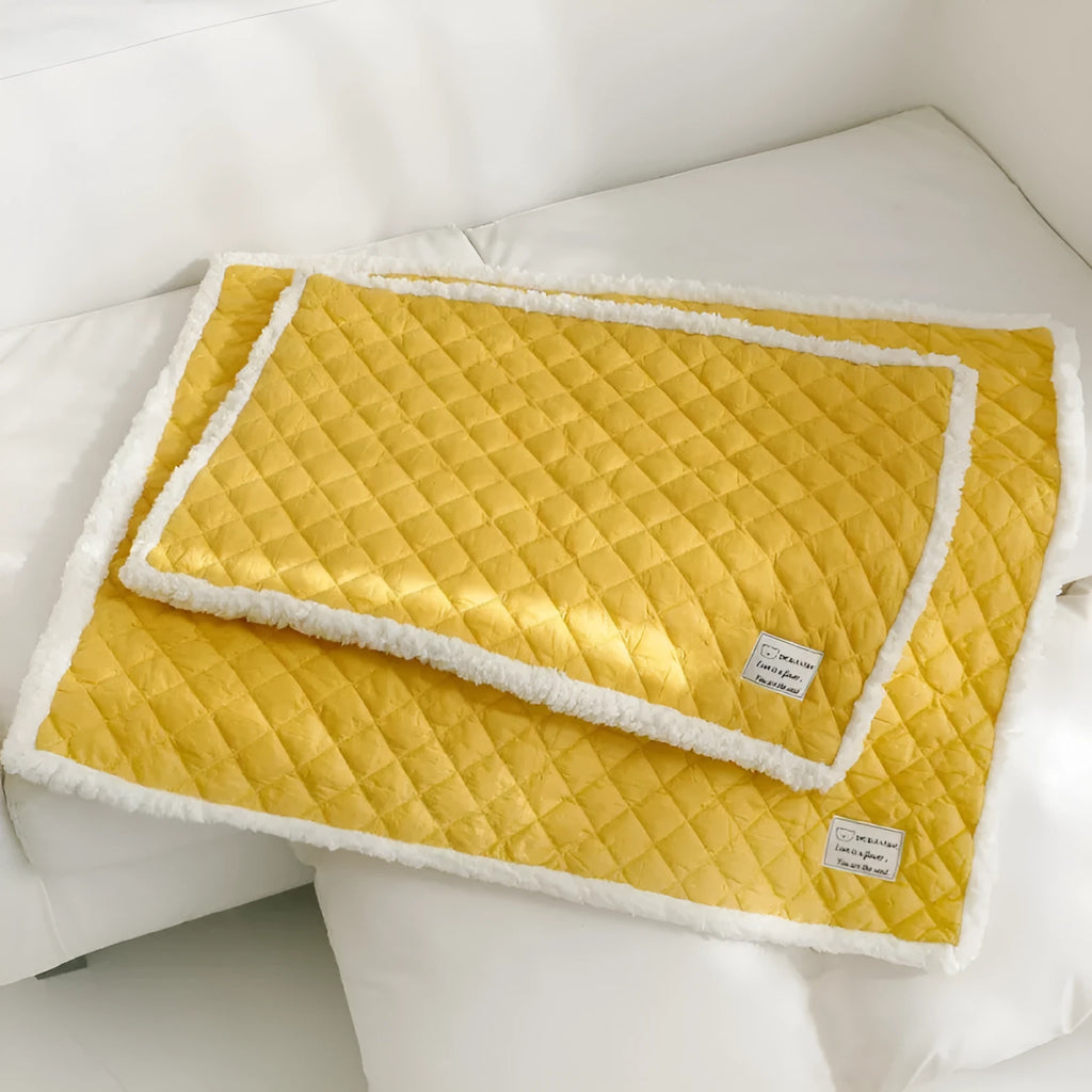 Blue quilted cloth pet blanket for cats lying flat, showing its rectangular shape and textured surface.