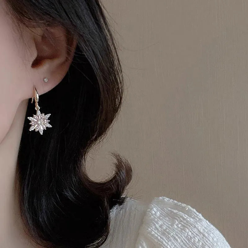 Gold alloy snowflake drop earrings with clear zircon centre on a white background