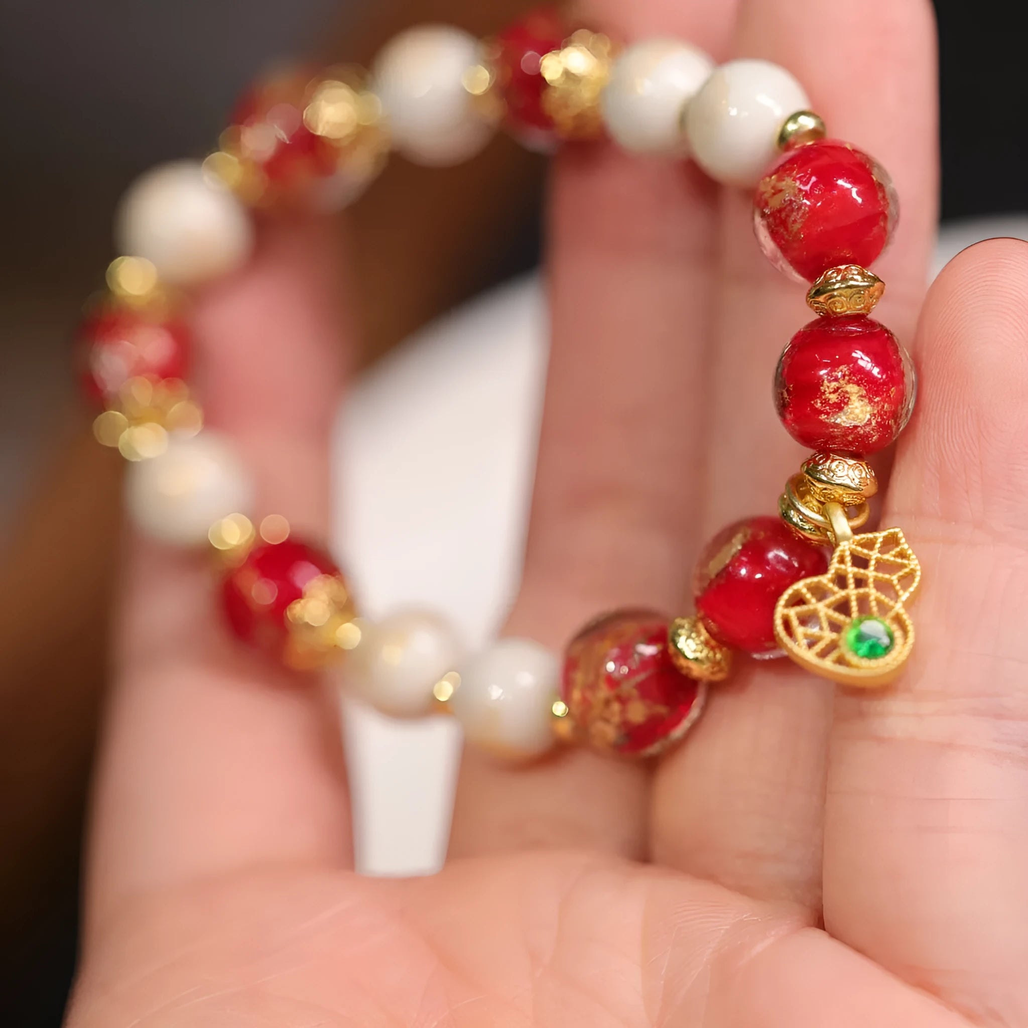 Women's ethnic style bracelet with gold foil designs on red and pink coloured glass glaze, featuring geometric shapes and charms.