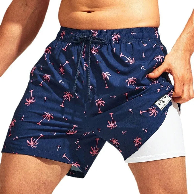 Man wearing loose green floral print boxer-style swimming trunks at the beach.