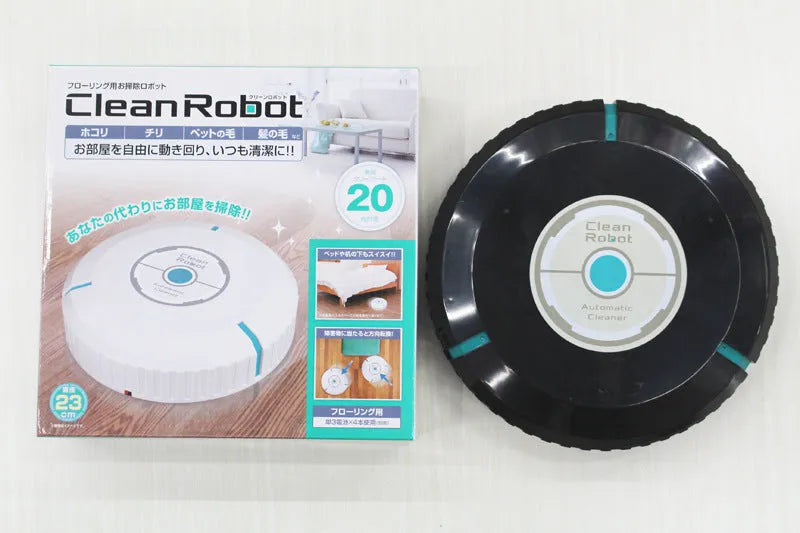 Black automatic sweeping robot on a wooden floor next to its packaging.