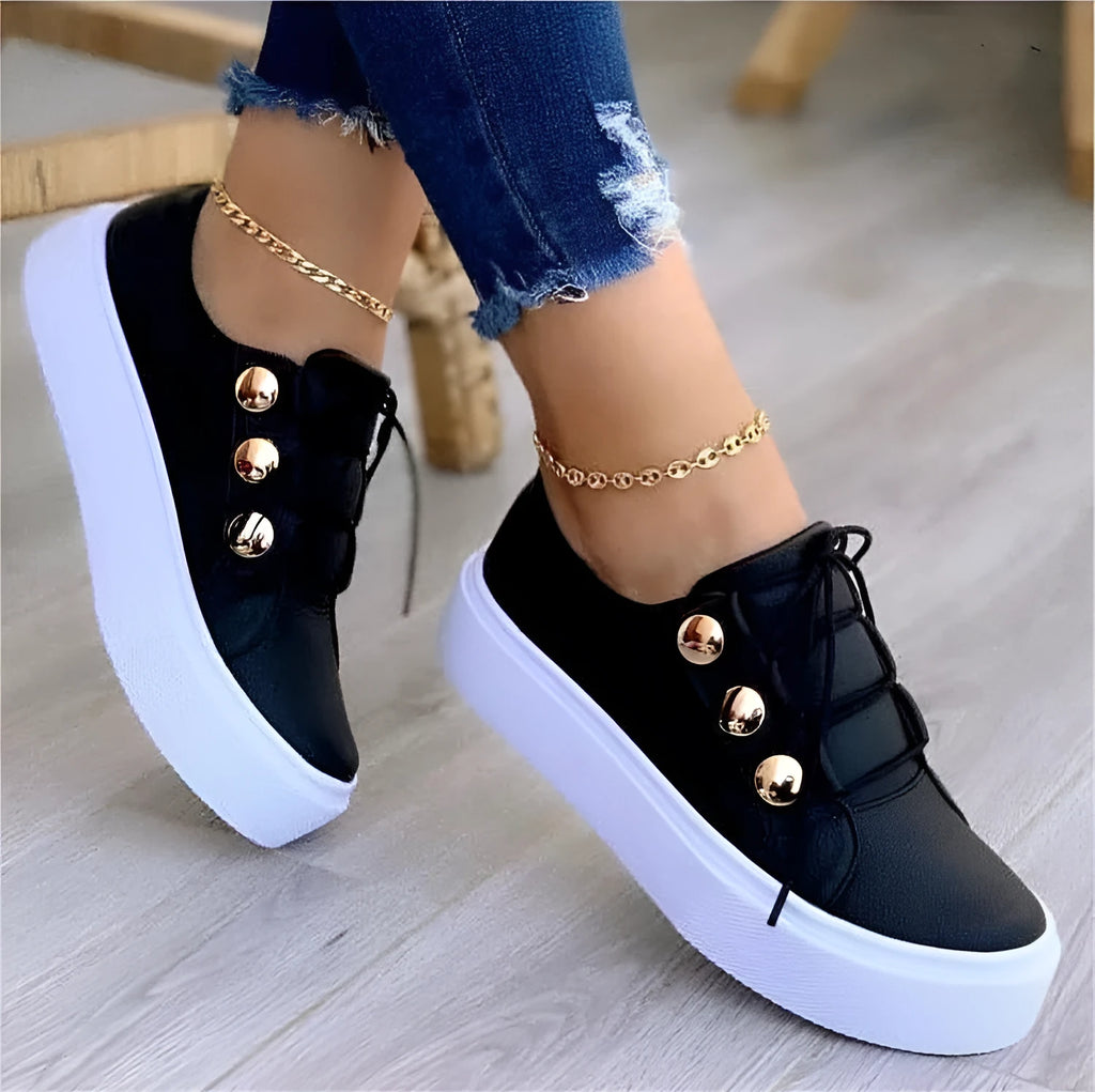 Women's white lace-up flat sneakers with silver rivet detail on the low upper and round toe.