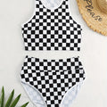 Adult woman wearing a black and white checkerboard print one-piece swimsuit with suspender straps and a backless sporty design.