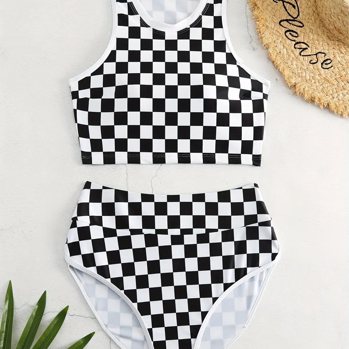 Adult woman wearing a black and white checkerboard print one-piece swimsuit with suspender straps and a backless sporty design.