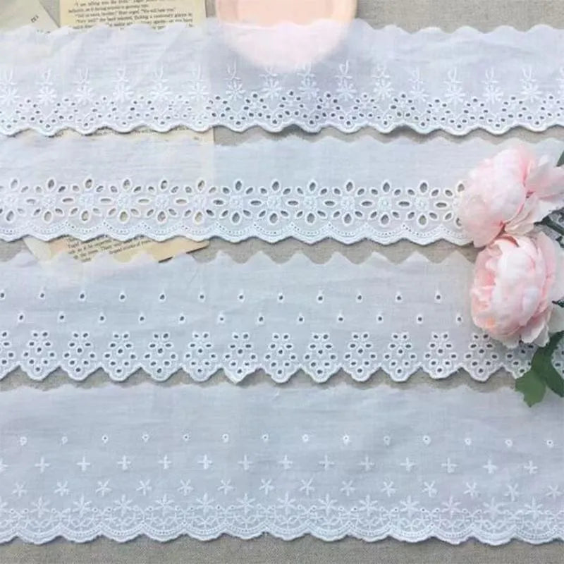 Roll of white cotton embroidery lace trim with cutout pattern, showing width variations.