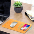 Brown leather wireless charging mouse pad with Micro USB port on a wooden desk.