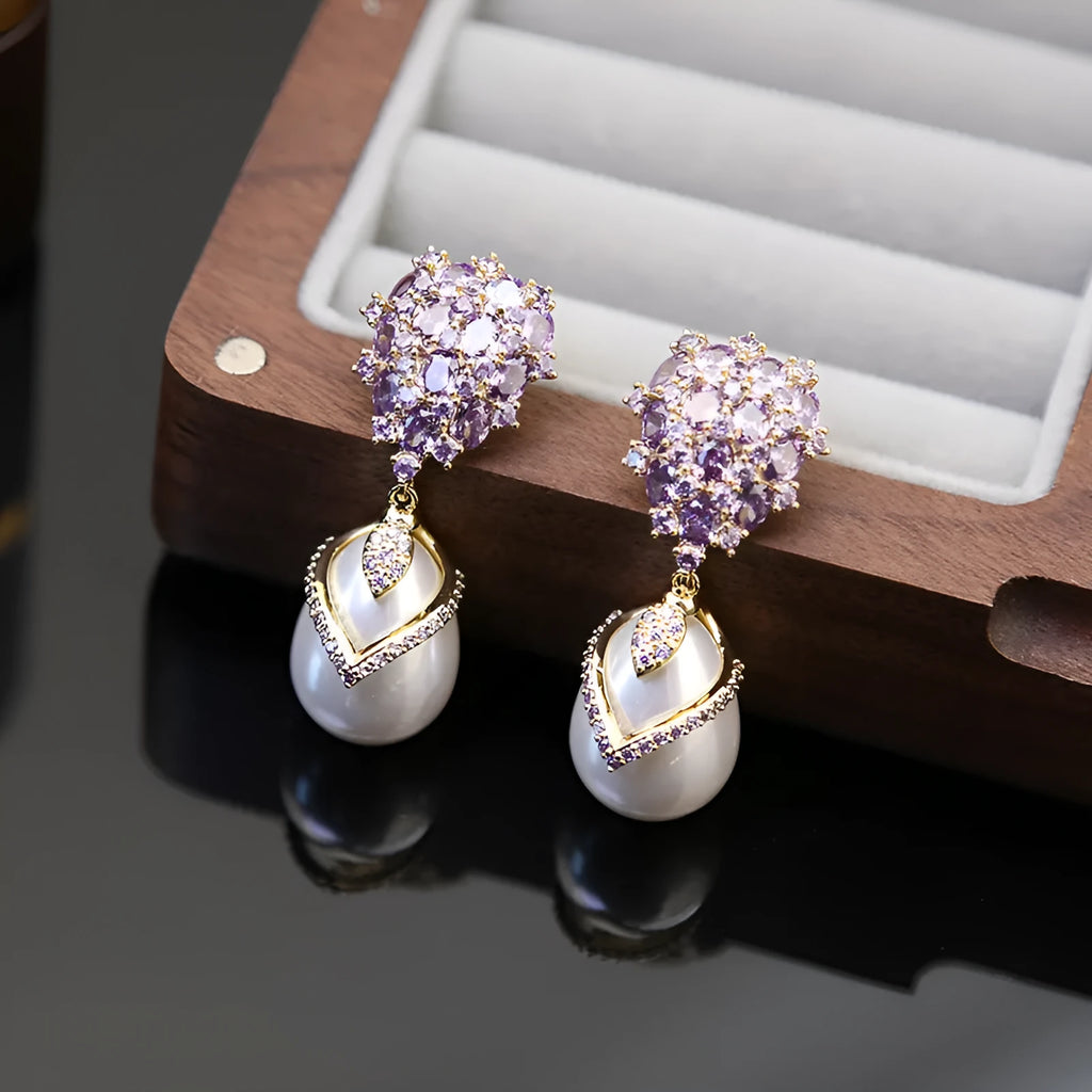 Close-up of a women's drop-shaped earring with inlaid pearl and zircon stones on an 18K gold-plated copper setting.