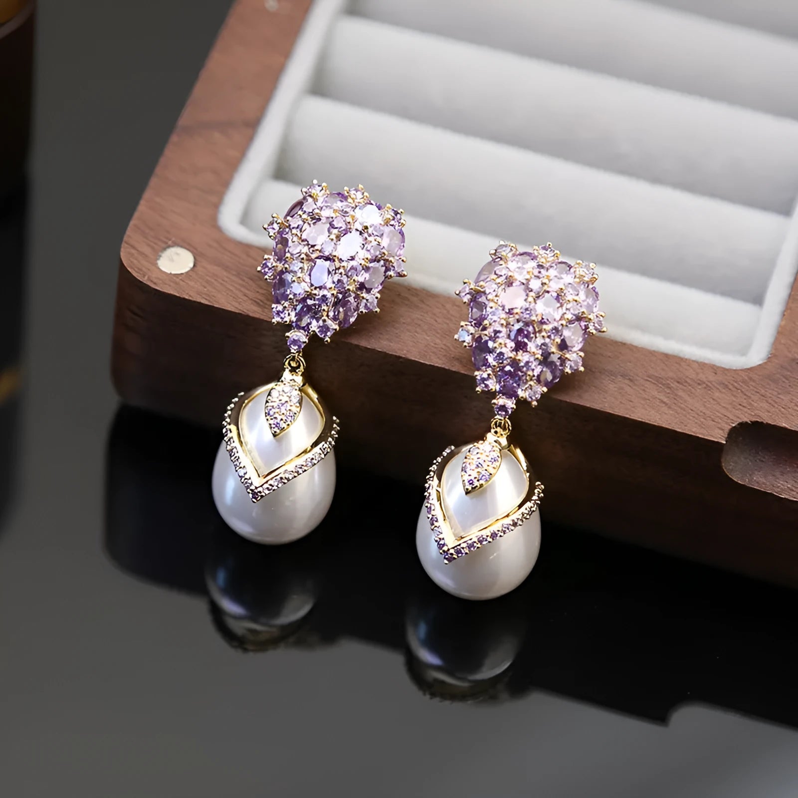 Close-up of a women's drop-shaped earring with inlaid pearl and zircon stones on an 18K gold-plated copper setting.