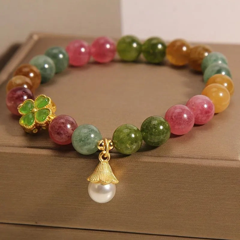 Natural colour tourmaline bracelet with four-leaf clover pearl pendant on wrist.