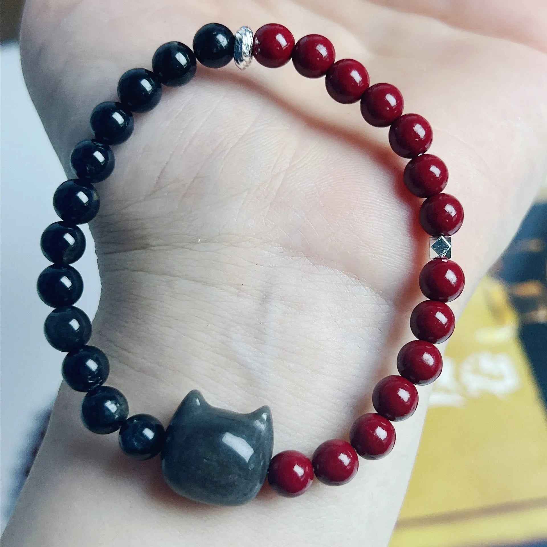 Handmade obsidian bead bracelet with a small cat charm on a cord.