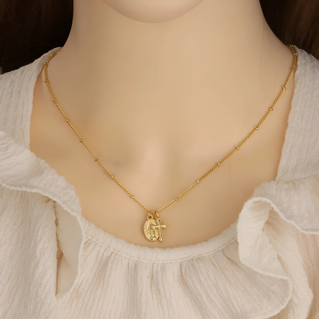Geometric gold Virgin Mary cross pendant necklace on a chain.