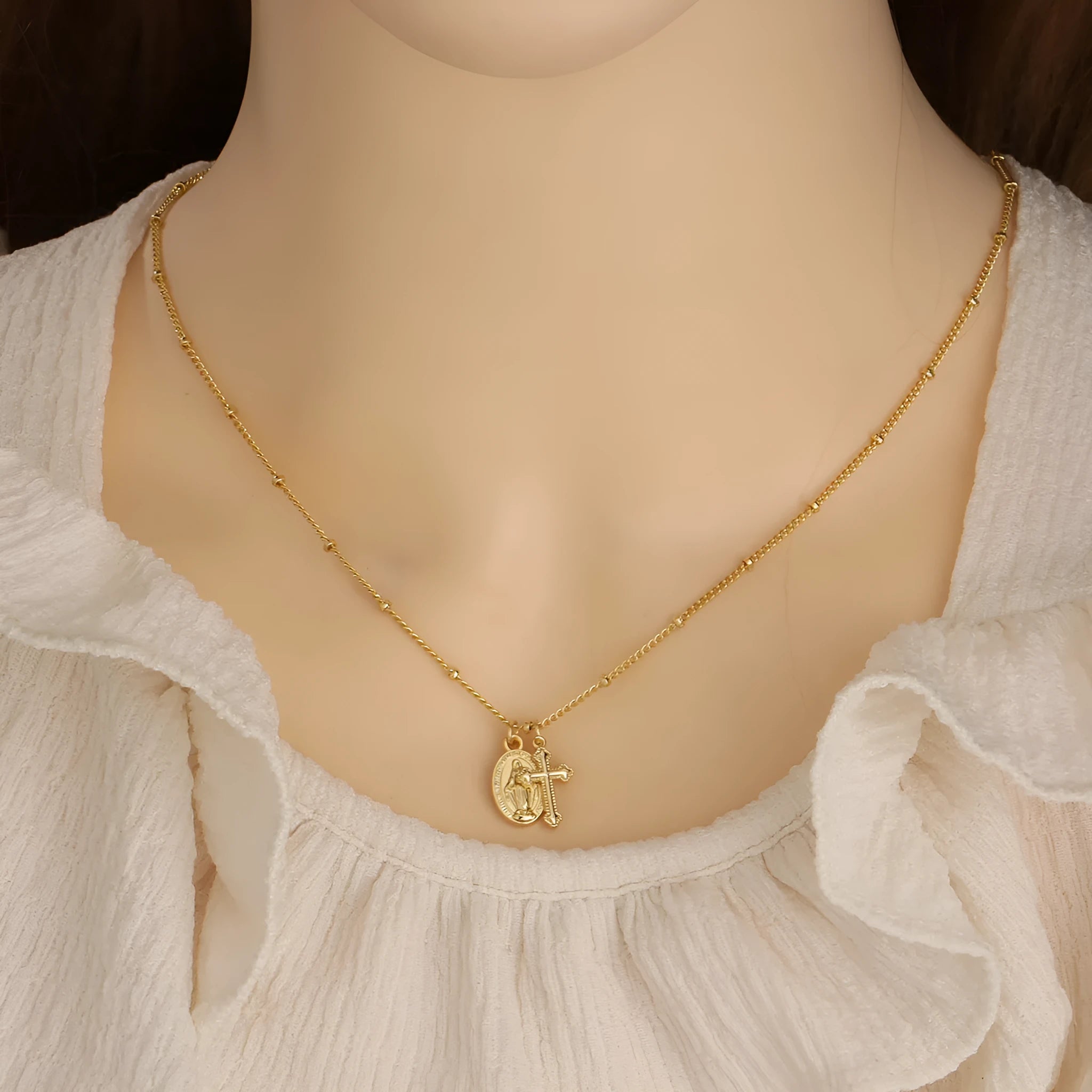 Geometric gold Virgin Mary cross pendant necklace on a chain.