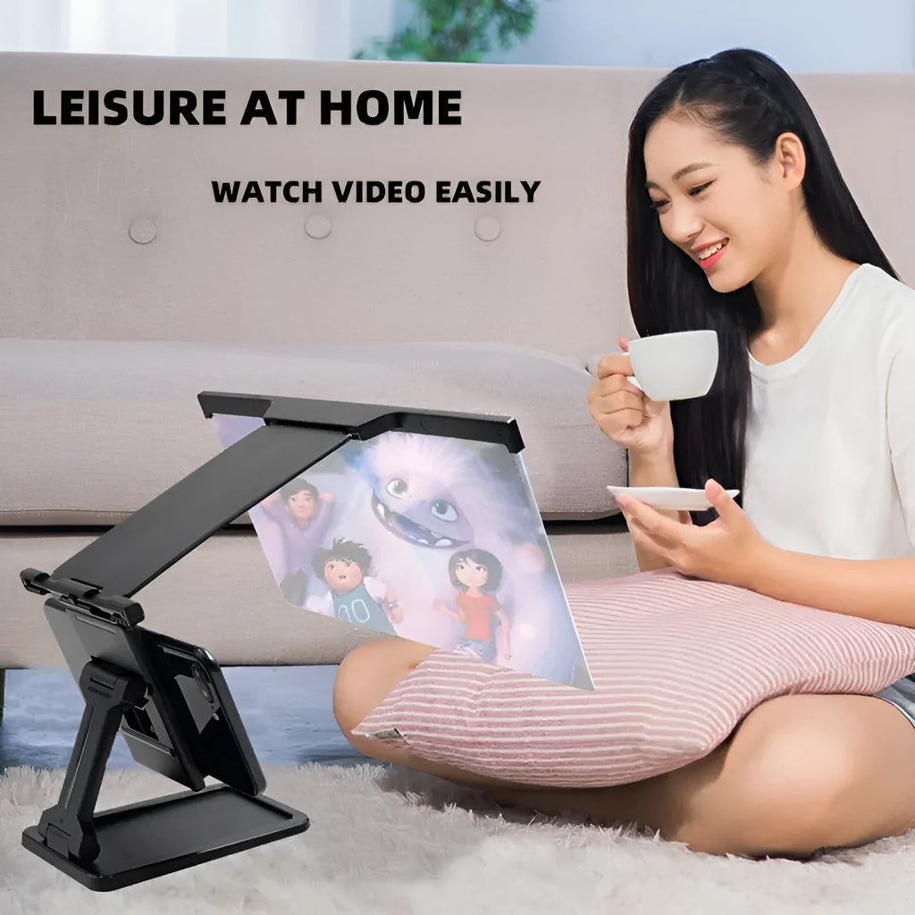 Black detachable mobile phone screen amplifier and folding holder shown on a desk next to a phone.