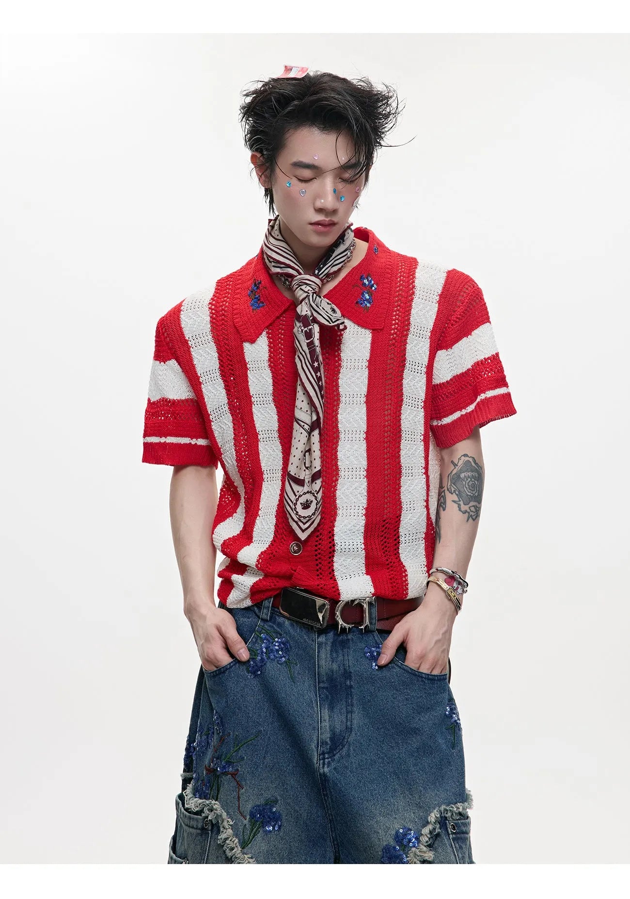 Man wearing a red and black patchwork striped knitted short sleeve shirt with a loose fit.