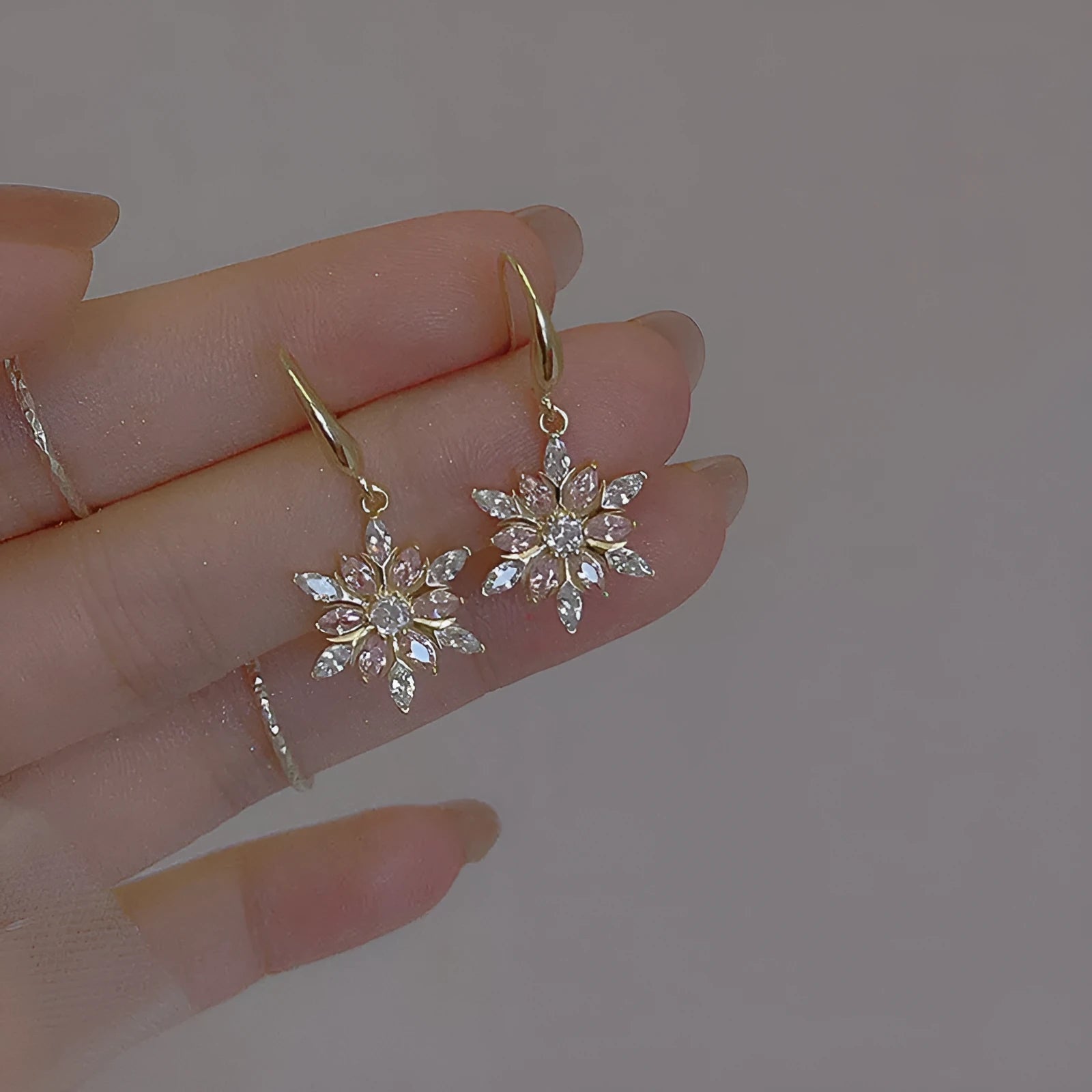 Gold alloy snowflake drop earrings with clear zircon centre on a white background