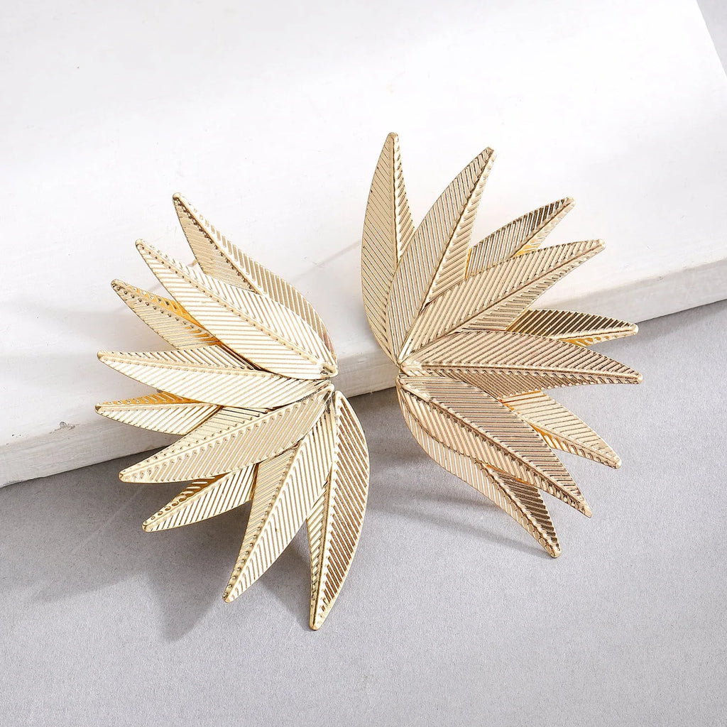 A pair of gold alloy drop earrings shaped like leaves, lying on a surface.