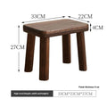 A rustic distressed wooden stool with bracket legs, used as a shoe changing bench in a hallway.