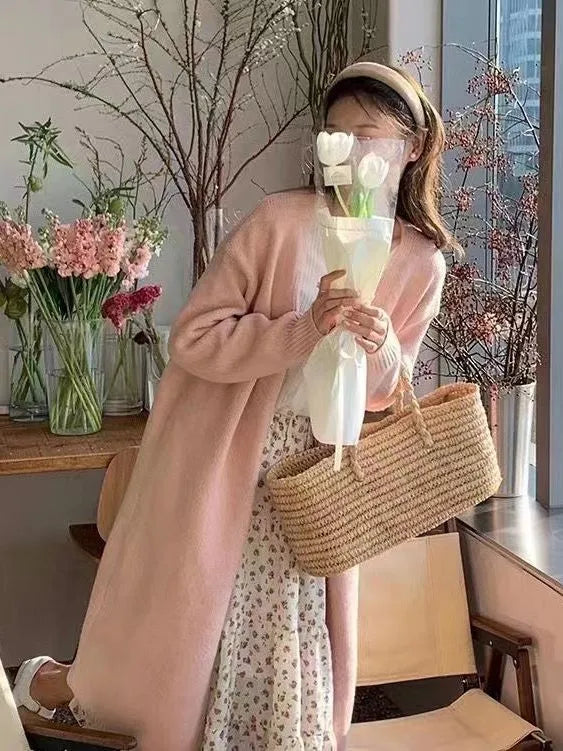 A woman wearing a khaki coloured, mid-length V-neck knitted cardigan with long sleeves.