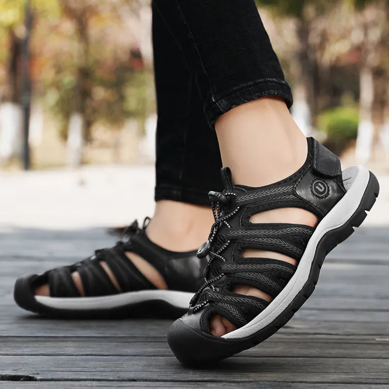Women's black leather mesh toe box sandals with elastic band and rubber sole on a beach
