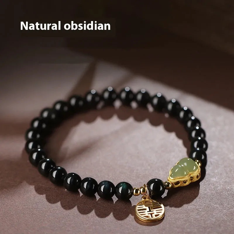 Black obsidian bracelet with a green Hetian jade gourd charm on a wrist.