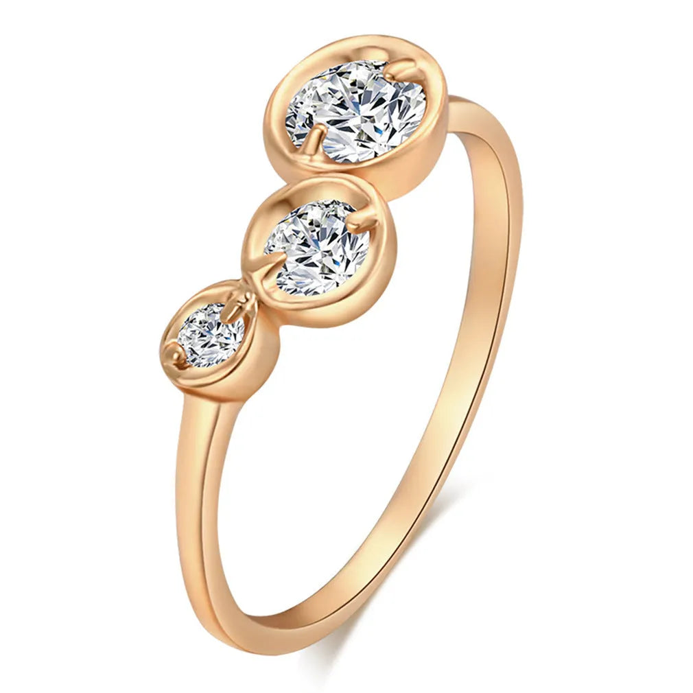 Three copper electroplated rings with lotus leaf design and round zircon stones in gold white zirconium tone on a flat surface
