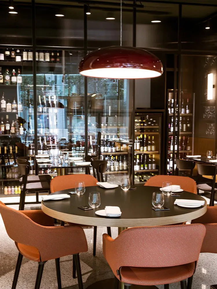 Modern Danish orange iron pendant lamp with adjustable cable over a restaurant dining table.
