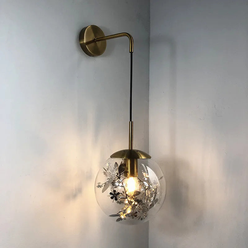 Modern round glass wall lamp in golden flower finish mounted beside a bed.