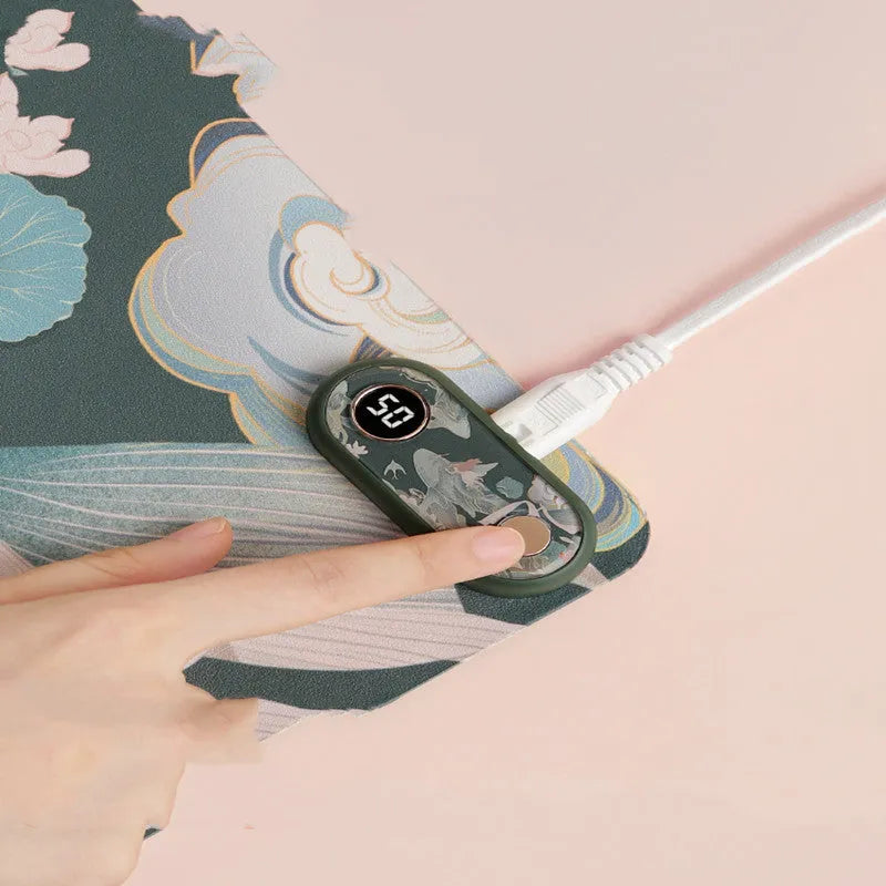 USB desktop heating pad on a desk, showing the fish leaping design on a grey PVC leather surface measuring 30 by 15 cm.