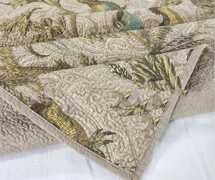 Blue American floral and bird pattern quilted cotton bedspread laid flat on a bed.
