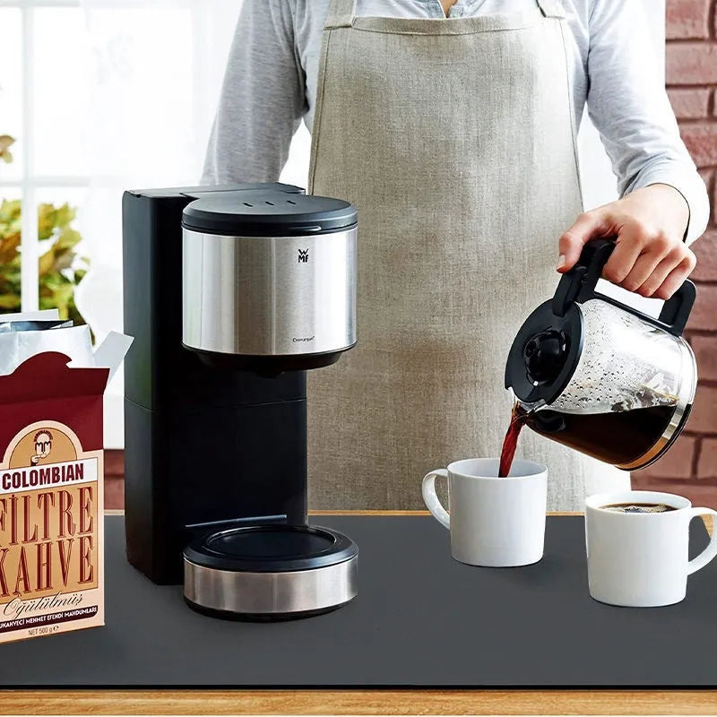 Square black kitchen drain mat with rubber backing placed under coffee machine on countertop