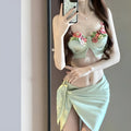 Green women's three-piece bikini swimsuit set with triangle top, briefs, and a short skirt on a mannequin.