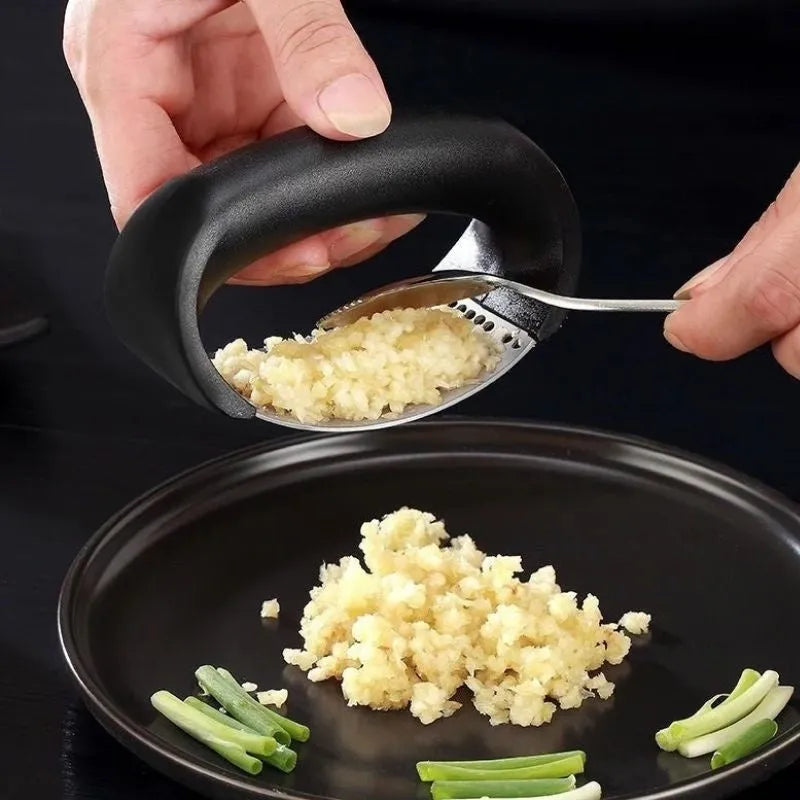 Stainless steel garlic press with ergonomic black handle on a kitchen counter.