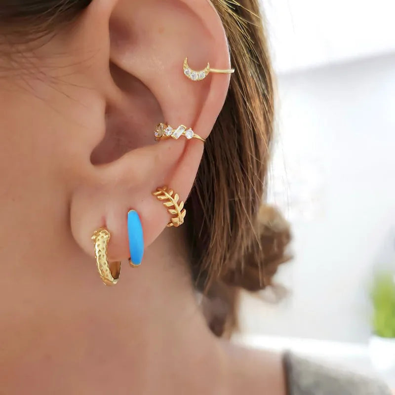 A pair of oval curved epoxy earrings in various colours with geometric ring details on a silver needle copper frame.