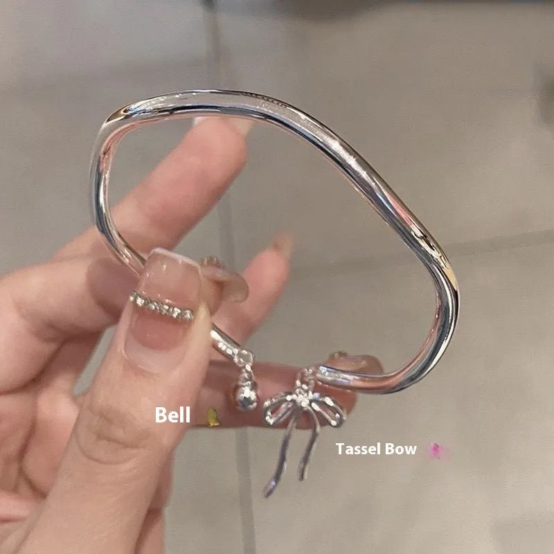 Close-up of a silver-toned adjustable bracelet with a bow bell charm on a model's wrist.