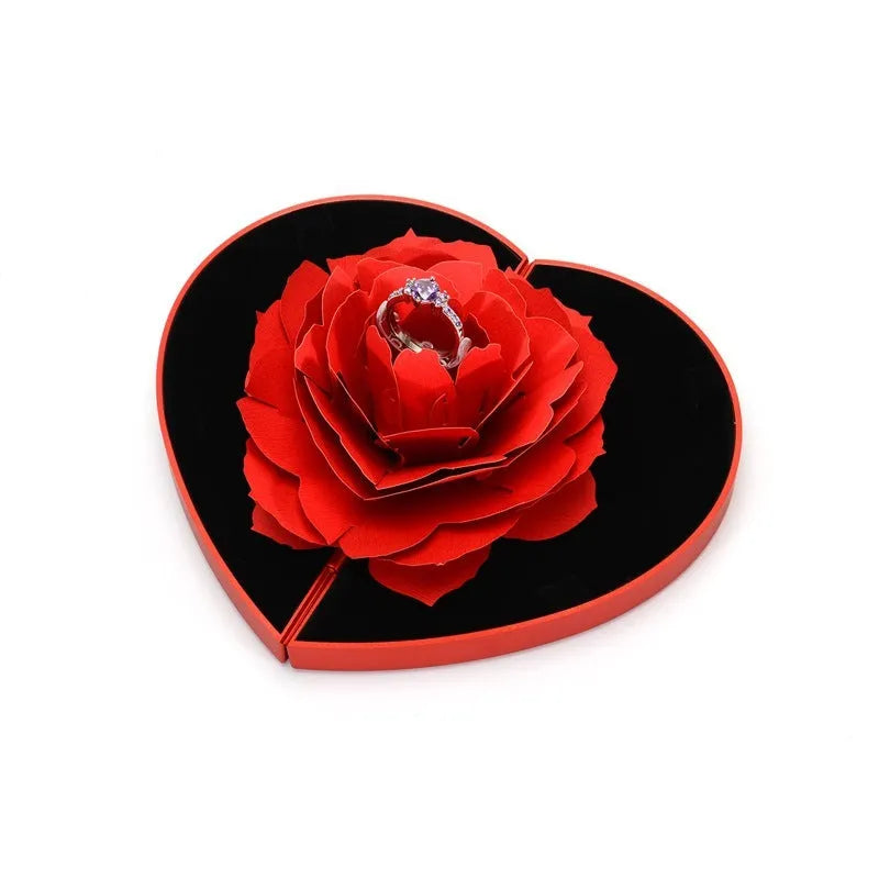 Red 3D heart-shaped plastic ring box with a rotating white rose decoration on top.