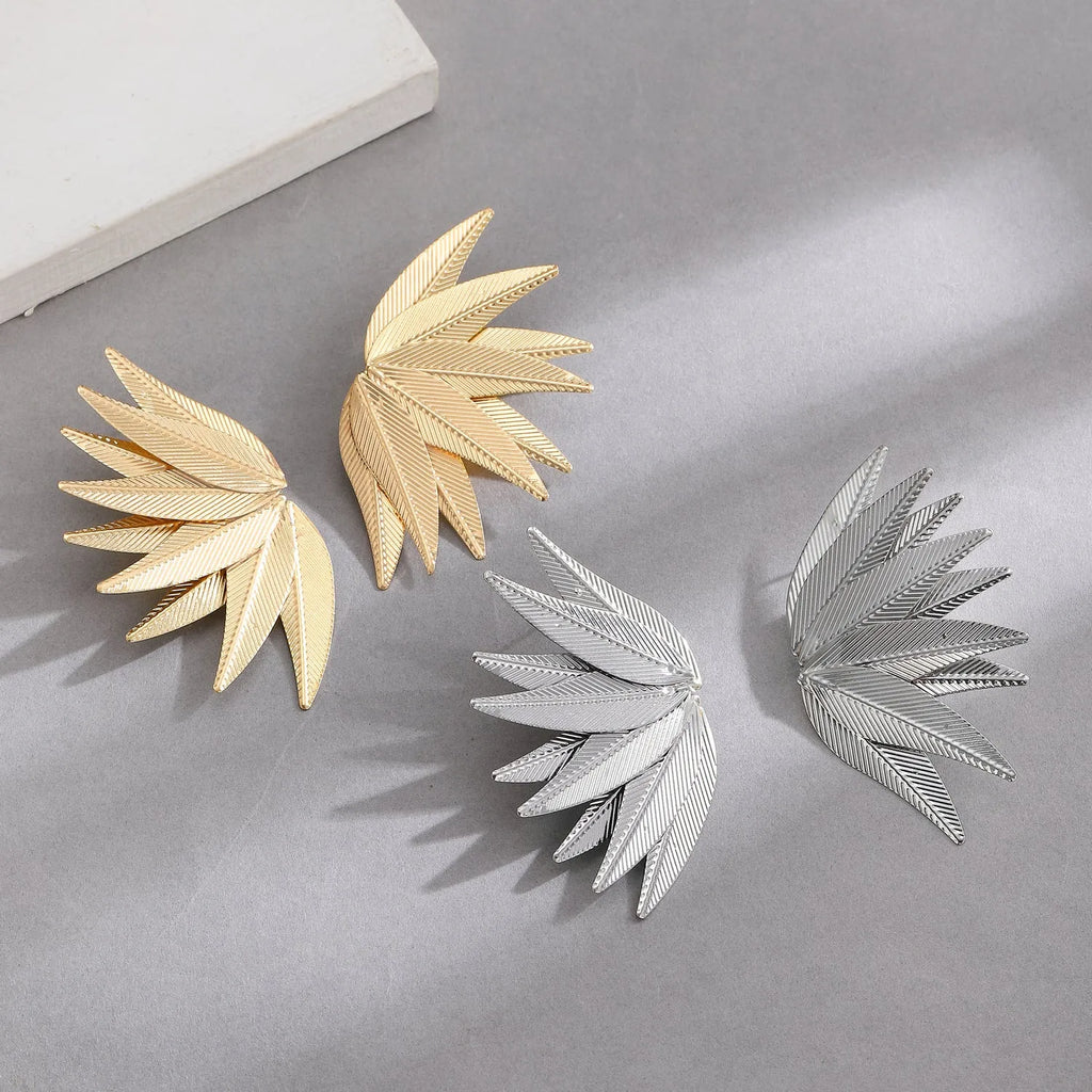 A pair of gold alloy drop earrings shaped like leaves, lying on a surface.